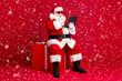 © deagreez - Full length photo of retired old man white beard hold netbook sit box take curious child present order wear santa x-mas costume sunglass headwear leather boot isolated red color background
