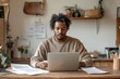 © Milos - A young man with dreadlocked hair sits at a desk with a laptop and scattered papers, emphasizing focus, productivity, and a creative work environment in a home office.