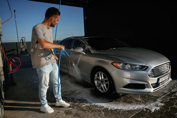 Silver colored surface, washing the automobile. Man is with his car outdoors