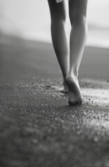 A close up of bare feet walking on a sandy beach, captured in black and white The horizon blurs in the background, enhancing the sense of tranquility and solitude