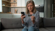 © Yuliia - Angry confused senior Caucasian woman mature elderly female mother hold credit card security problem using bank app for payment retired grandparent mobile phone scam money loss failure error home sofa