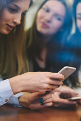 Wall Mural - Young women searching information on content websites during leisure time on publicity area, attractive hipster girls using 4g wireless connection on cellular phones for updating profile online