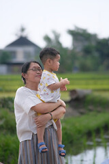 A middle-aged woman carrying her son walking around the rice fields