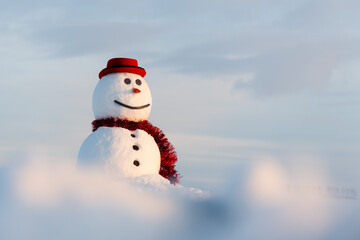 Wall Mural - Funny smiley snowman in stylish red hat and red scarf on snowy field. Blue sky on background