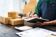 © NanSan - A man is working at his desk, preparing parcel boxes for shipment. He checks and packs items carefully, using shockproof materials, and attaches labels before sending them to customers via EMS.