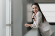 © EduLife Photos - Smiling Businesswoman Leaning by Office Window. A cheerful businesswoman leans against a window in a modern office, exuding confidence and positivity, representing leadership and success.