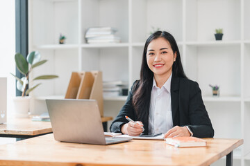 Wall Mural - confident businesswoman smiles while working at her desk, showcasing modern office environment. She is engaged with her laptop and notes, reflecting professionalism and productivity.