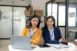© ArLawKa - Two Asian women work online with laptop and smartphone. A joyful moment captured as two female colleagues laugh together during a productive meeting in the office.