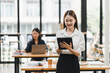 © PRIME STOCK LAB - young woman in striped shirt smiles while using tablet in modern office setting, showcasing productive atmosphere. In background, another woman works on laptop, emphasizing collaboration and focus.