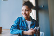 © BullRun - Cheerful african american woman dressed in jeans jacket using electronic headphones and smartphone internet connection for listening positive audio book, happy girl enjoying leisure time indoors