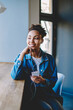 © BullRun - Positive female teenager looking away and dreaming about big love while listening romantic music song via electronic earphones, happy woman holding cellular gadget and enjoying time in coffee shop