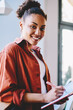 © BullRun - Half length portrait of cheerful african american female writer smiling at camera while spending time in university campus, positive hipster girl with knowledge textbook in hand in cafeteria