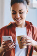 © BullRun - Happy dark skinned hipster girl sending sms message via smartphone device while enjoying caffeine beverage, african woman holding paper cup with coffee and reading article on content funny website