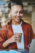 © BullRun - Portrait of cheerful female freelancer sitting at table with modern laptop computer and smiling at camera during distance job in coworking space, happy woman enjoying coffee break from remote work