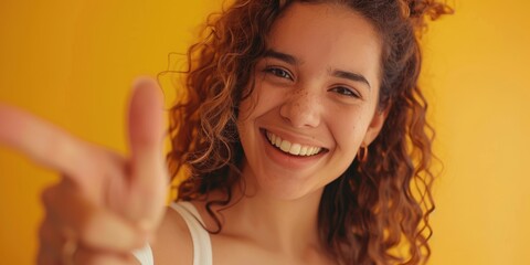 Joyful portrait of a woman in a studio, smiling with a positive expression and pointing gesture against a yellow background