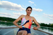 © Connect Images - Confident woman rowing a boat on a serene lake with a clear blue sky and lush greenery in the background.