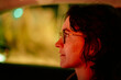 © Connect Images - Side profile of a smiling young adult wearing glasses in a dimly lit car interior at night.