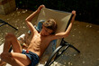 © Connect Images - Young boy relaxing on a sun lounger in a sunlit courtyard, enjoying the warmth with eyes closed.