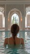 © Maria Mikhaylichenko - Woman relaxing in luxurious indoor pool, gazing through ornate Moroccan-style arched window at lush greenery outside. Tranquil spa atmosphere exudes serenity.