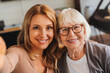 © InsideCreativeHouse - Senior woman sitting together with her daughter on couch and taking selfie with smartphone at home