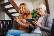 © InsideCreativeHouse - Senior women using digital tablet and middle aged woman, her daughter, mobile phone while relaxing on sofa at home