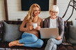 © InsideCreativeHouse - Smiling senior woman and her middle aged daughter sitting relax on sofa and drinking coffee in living room watching video on laptop together