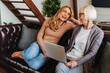© InsideCreativeHouse - Laughing senior mother and daughter using laptop while having rest at home on sofa