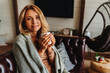 © InsideCreativeHouse - Middle aged woman relaxing at home with cup of coffee while sitting on sofa and covers with blanket. Looking in camera