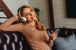 © InsideCreativeHouse - Attractive adult woman siting on couch with smartphone and headphones listening music