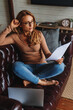 © InsideCreativeHouse - Middle aged woman using laptop and reading documents while working remotely at home
