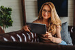 © InsideCreativeHouse - Middle aged woman sitting on sofa in living room and using digital tablet