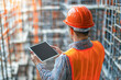 © Kowit - A man wearing an orange safety vest and a hard hat is holding a tablet