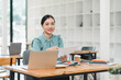 © PRIME STOCK LAB - young woman in teal blouse sits at wooden desk, smiling while holding documents. modern office setting features laptop, notebooks, and coffee cup, creating productive atmosphere.