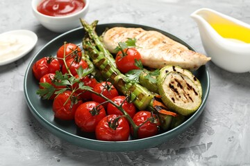 Delicious grilled vegetables and chicken breast served on grey textured table, closeup