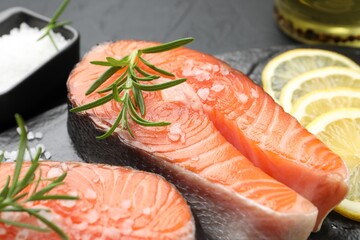 Fresh raw salmon steaks with salt, lemon and rosemary on dark table, closeup