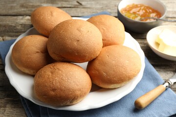 Wall Mural - Fresh tasty buns, jam and butter on wooden table, closeup