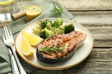 Tasty grilled salmon steak, lemon, broccoli and rosemary on wooden table, closeup