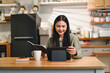 © PRIME STOCK LAB - woman is sitting at wooden kitchen table, smiling while using tablet and reading book. cozy kitchen features various appliances and decor, creating warm atmosphere.