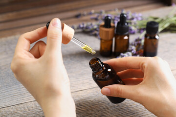 Wall Mural - Woman using essential oil at wooden table, closeup