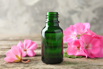 Wall Mural - Bottle of geranium essential oil and beautiful flowers on wooden table, closeup