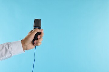 Wall Mural - Man with microphone on light blue background, closeup. Space for text