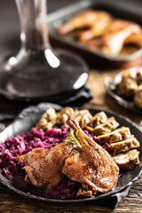 Portion of roast duck leg red cabbage homemade dumplings on plate and red wine on the background