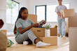© Drazen - Young black woman unpacking cardboard boxes while moving into new home with her boyfriend.