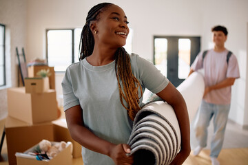 Happy black woman and her boyfriend carrying carpet in their new apartment.