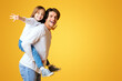 © Prostock-studio - Cheerful Funny Father Playing With His Happy Little Girl, imitating airplane, yellow background, panorama with empty space