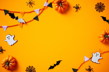 Halloween flat lay composition with pumpkins, spiders, ghosts, bunting flag garland on orange background. Happy Halloween banner mockup.