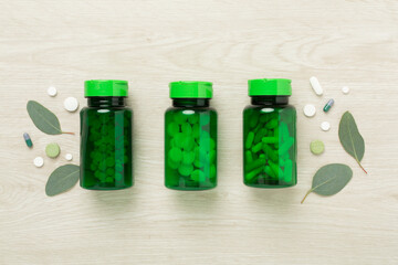 Sticker - Bottles with pills and green leaves on wooden background, top view