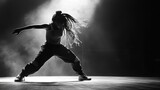 A female dancer with dreadlocks performs a hip hop dance move in a spotlight.