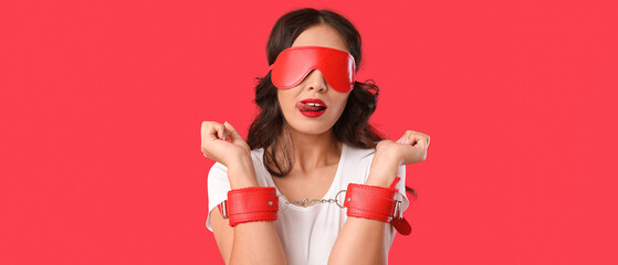 Wall Mural - Beautiful young sexy Asian woman with handcuffs and mask on red background