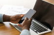 © Prostock-studio - Unrecognizable black businessman holding smartphone with black screen and using laptop at workplace in office, closeup with copy space